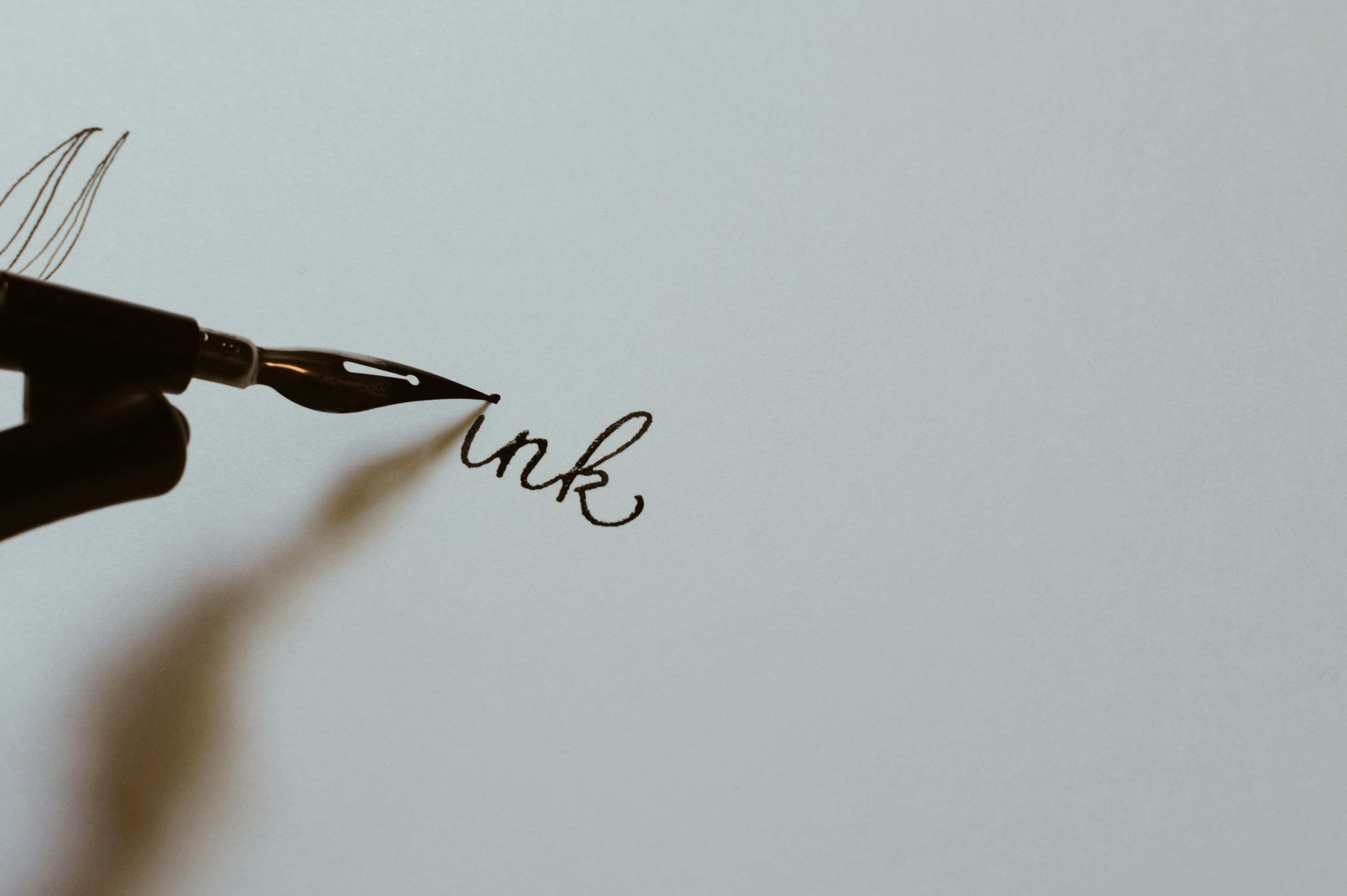 A calligraphy pen mid-stroke, writing the word ink on paper